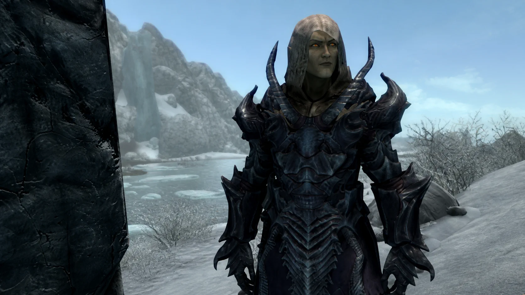 A close portrait of the unmasked Altmer necromancer wearing dark heavy armor in the snow